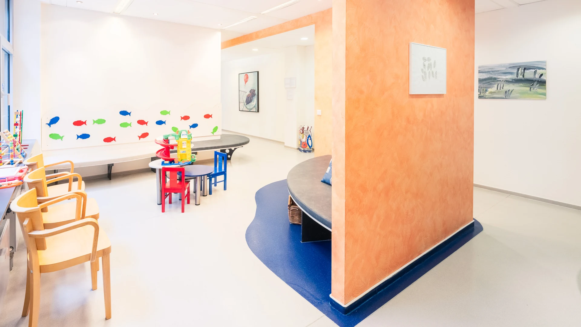 Wartezimmer mit Kindertisch, Holzstühlen und bunten Fischen an der Wand