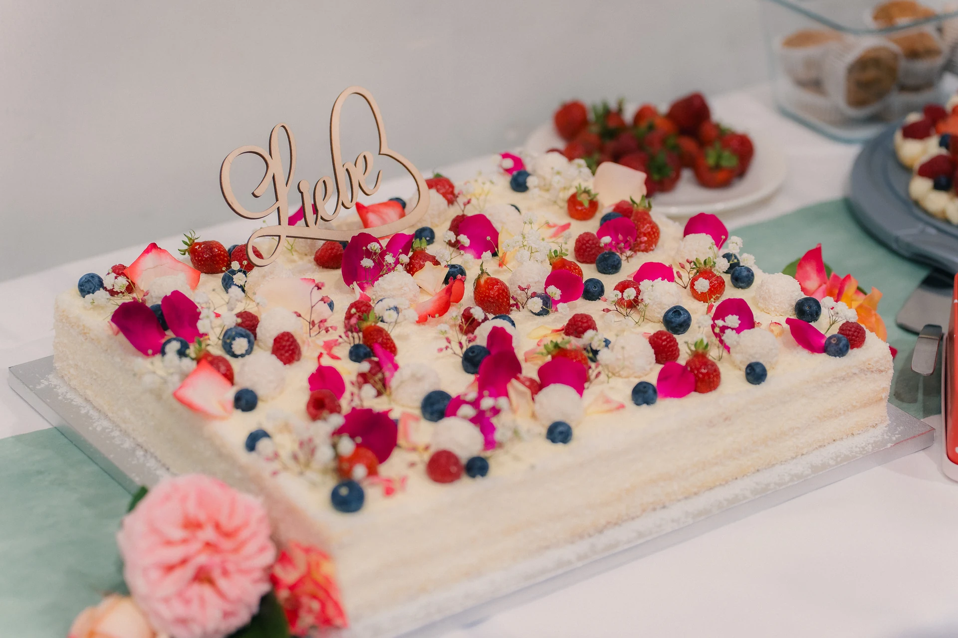 Hochzeitstorte mit Beeren und Blüten und einem Schriftzug „Liebe“