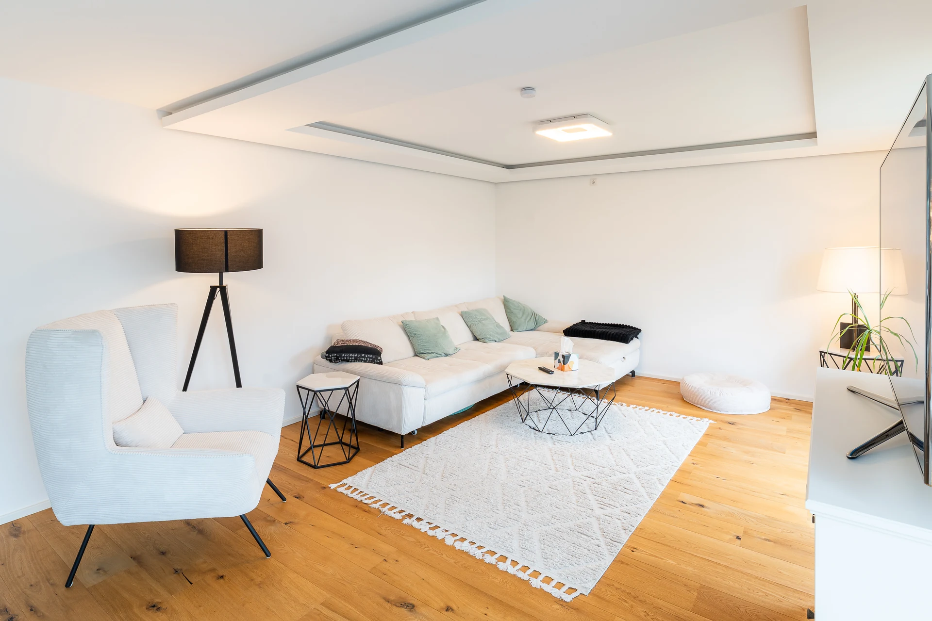 Wohnzimmer mit weißem Ecksofa, Sessel und Stehlampe auf Eichenparkett