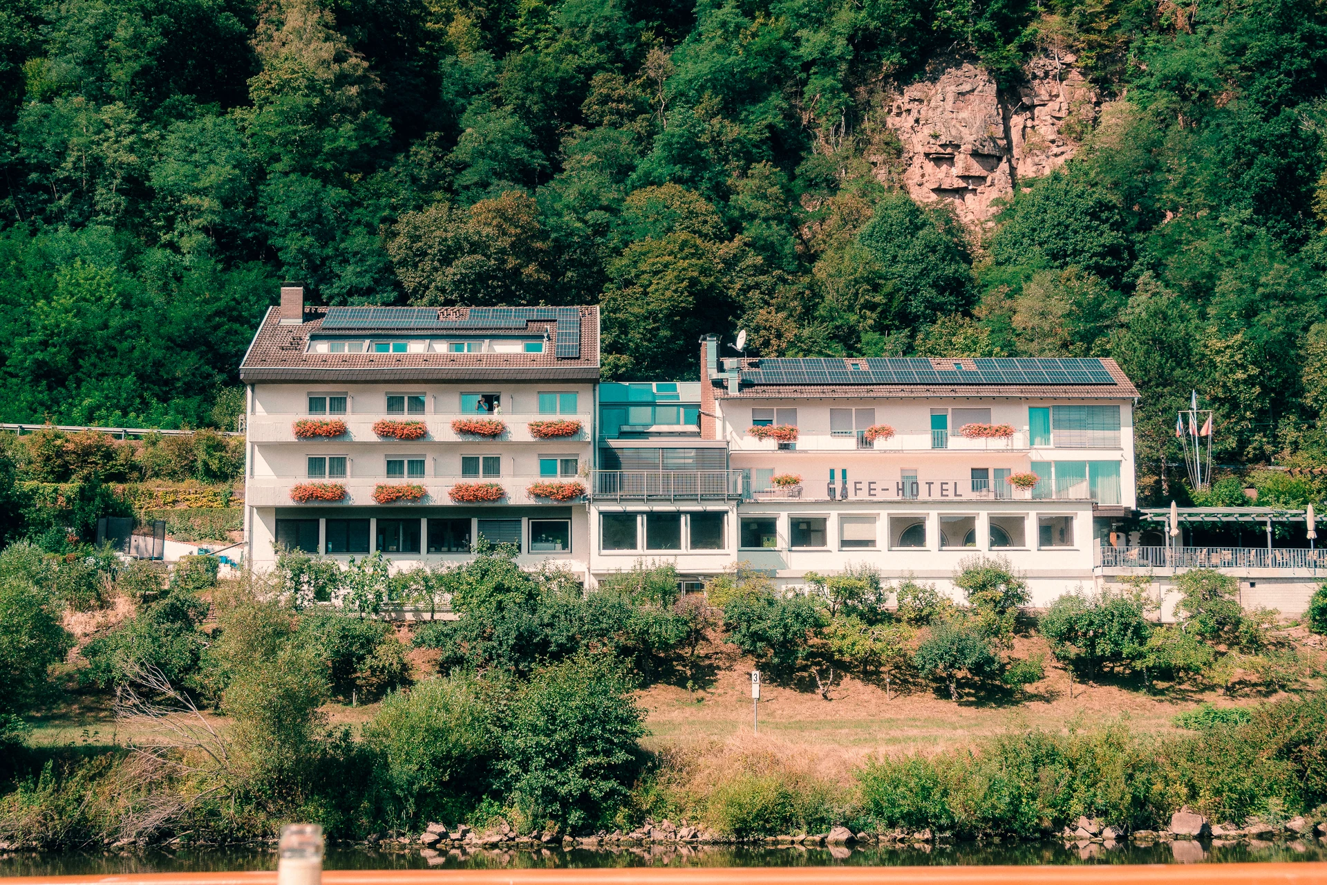 Hotel mit Blumenkästen am bewaldeten Ufer im Neckartal