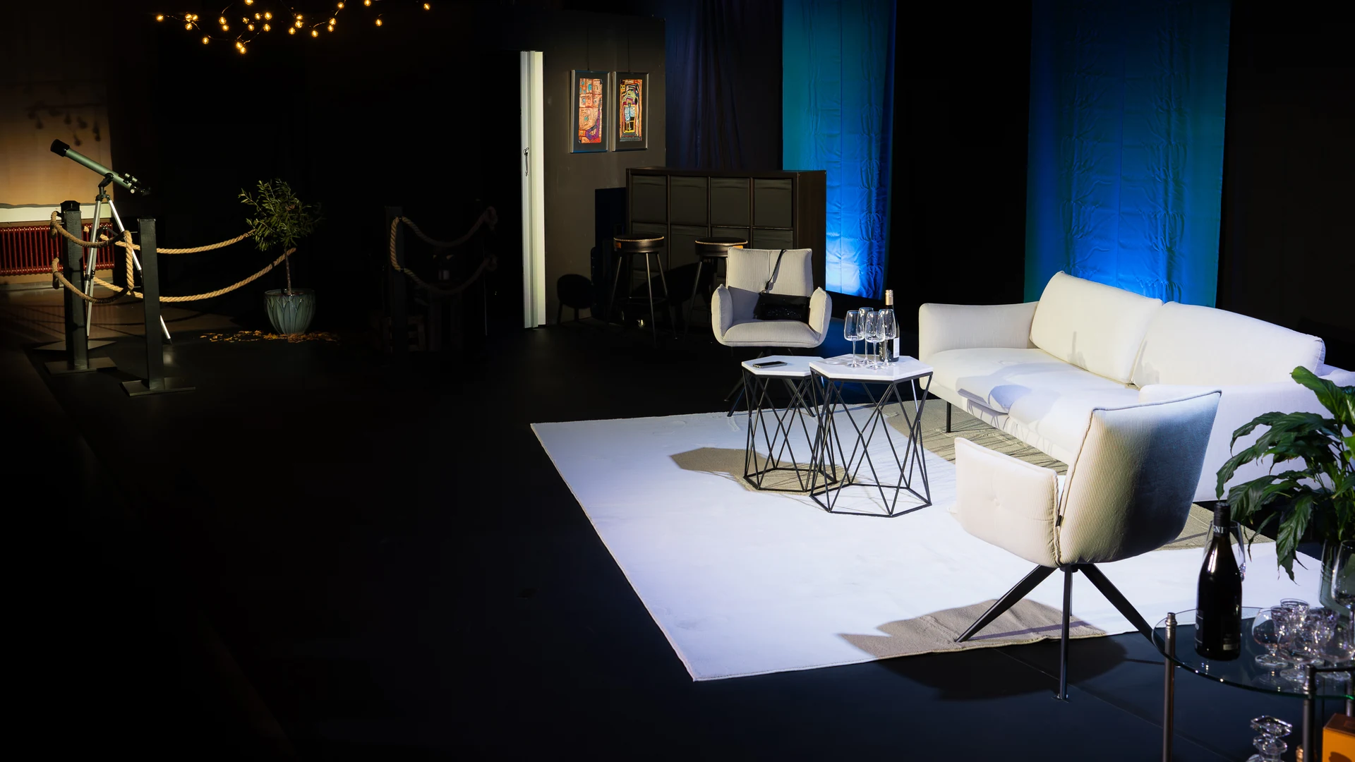 Leeres Bühnenbild mit weißem Sofa, Sesseln und Lichterkette vor blauen Vorhängen